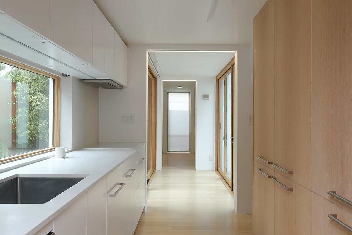 Compact kitchen beside a glass-enclosed bridge connecting the two volumes of the Evelyn ADU
