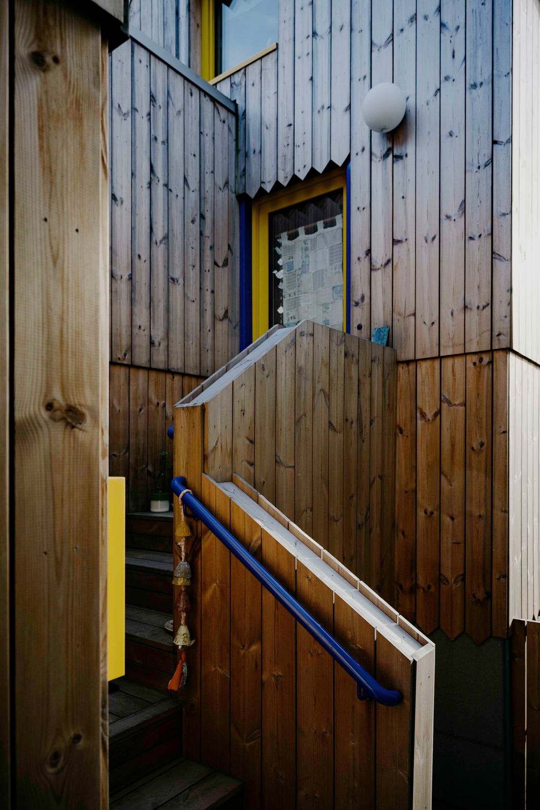 Wood-clad exterior entry stair with a blue steel handrail leading to a yellow-framed door on a Seattle ADU