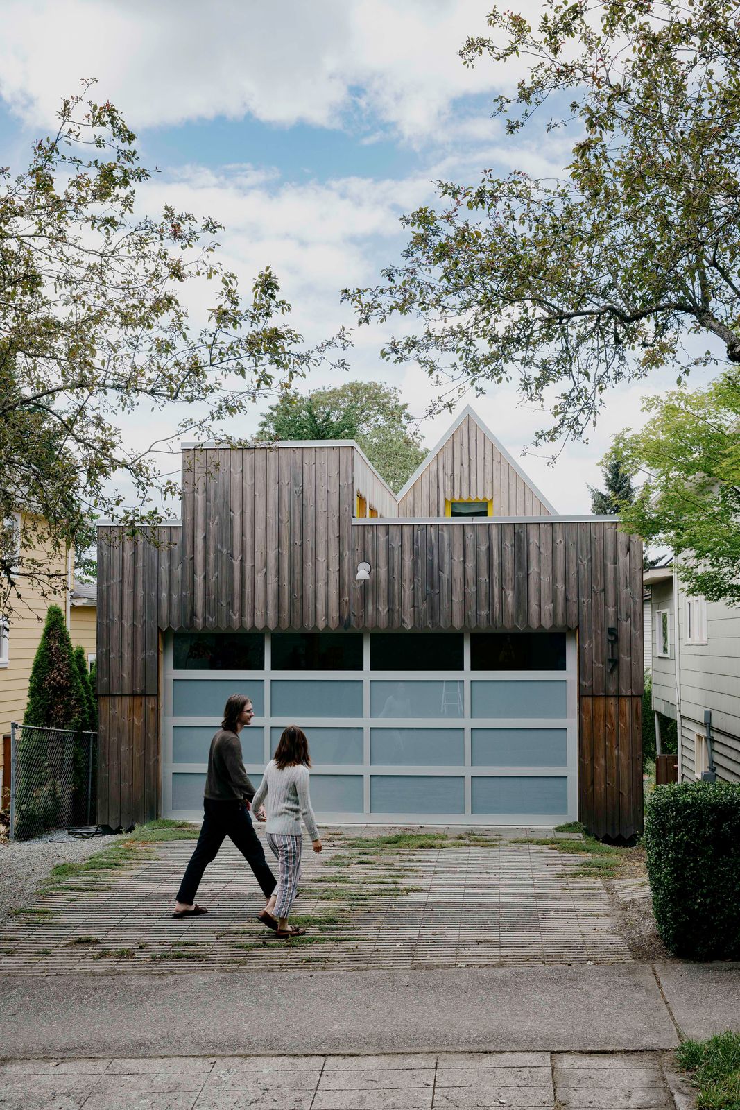 Street view of a Seattle garage ADU with a frosted glass garage door, dark vertical wood siding, and twin gables behind