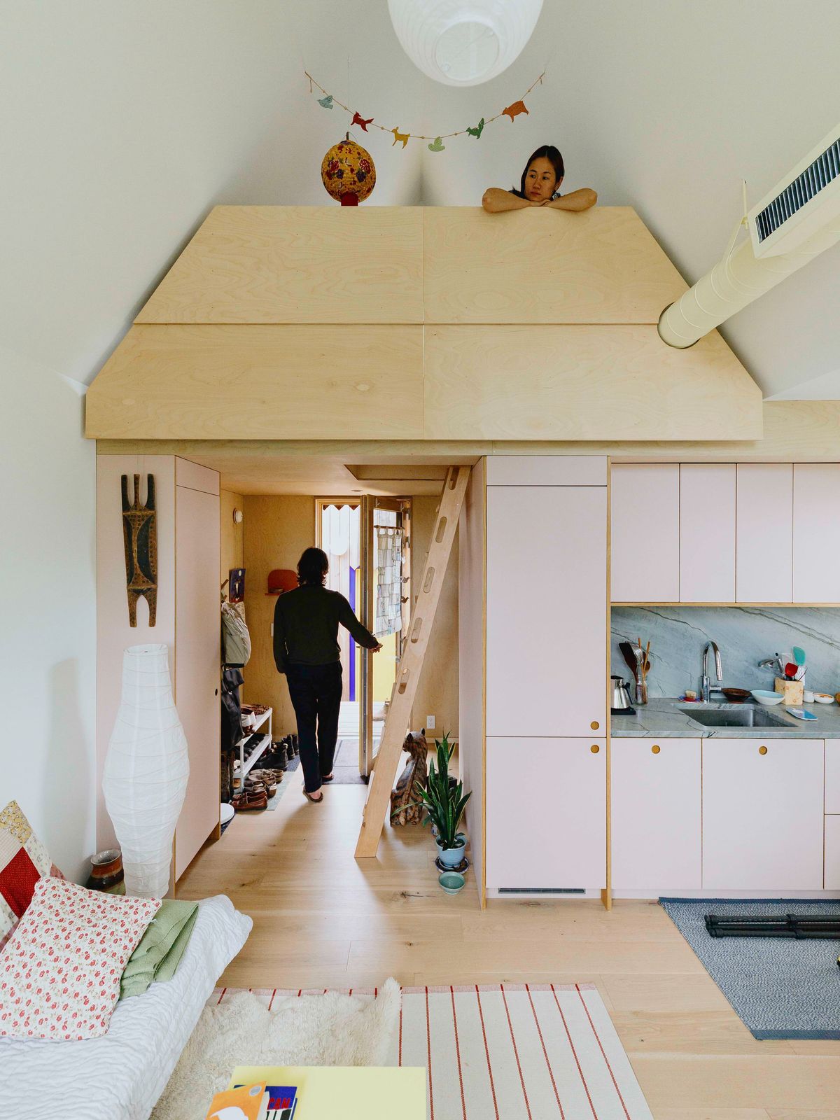 Interior of a Seattle ADU with pink kitchen cabinets, a stone backsplash, and a plywood sleeping loft reached by a ladder